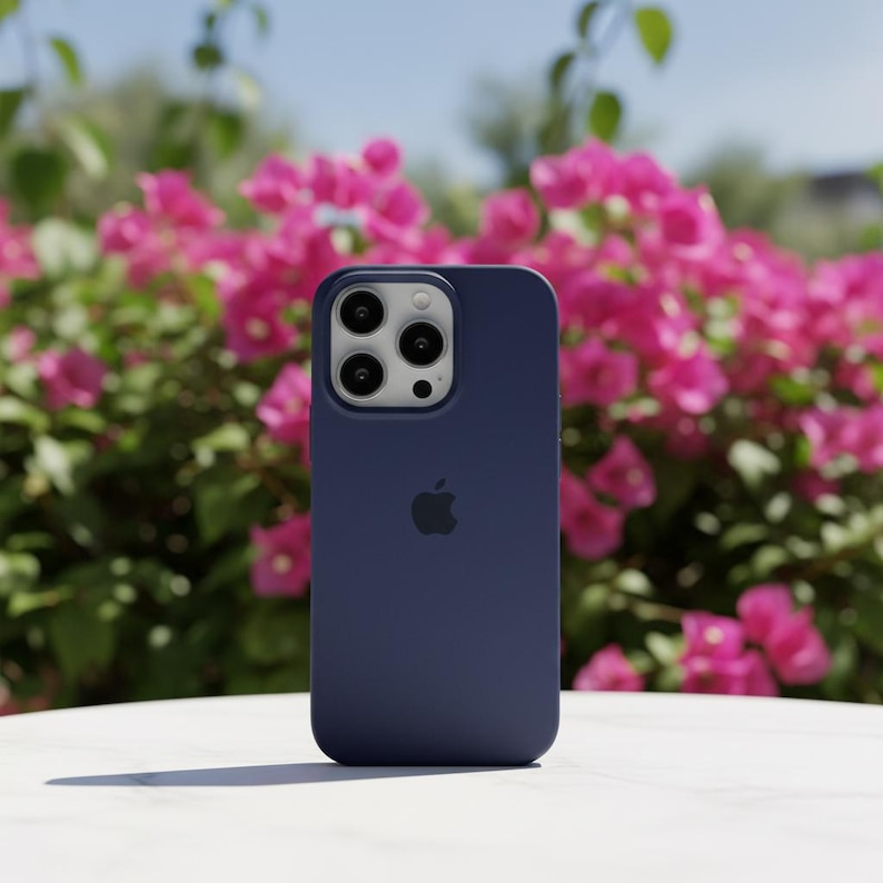 May include: A navy blue smartphone case with a triple-lens camera system and the Apple logo. The case is made of a smooth material and is set against a backdrop of pink flowers and a clear blue sky.