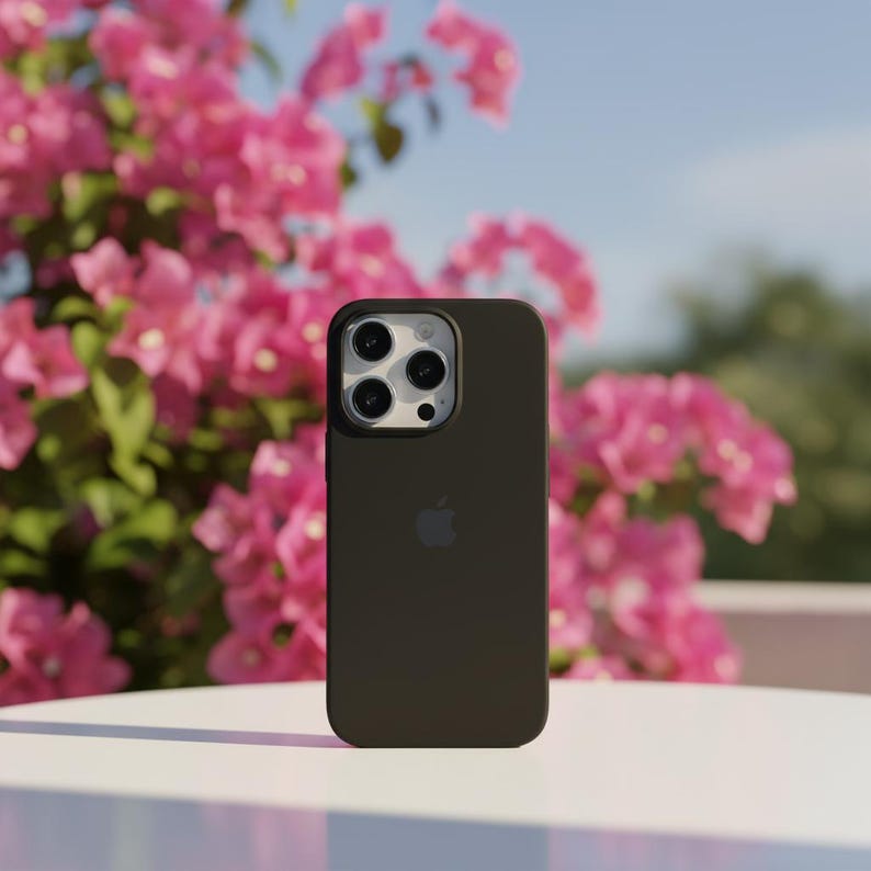 May include: A dark brown smartphone case with a camera module and the Apple logo. The case is shown against a backdrop of pink flowers and a blue sky.