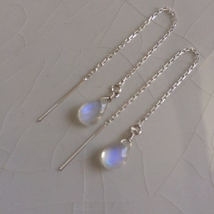 May include: A pair of silver dangle earrings with moonstone teardrop charms. The earrings have a delicate chain design.