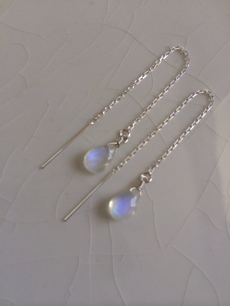 May include: A pair of silver dangle earrings with moonstone teardrop charms. The earrings have a delicate chain design.