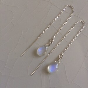May include: A pair of silver dangle earrings with iridescent moonstone teardrop charms. The earrings have a delicate chain design.
