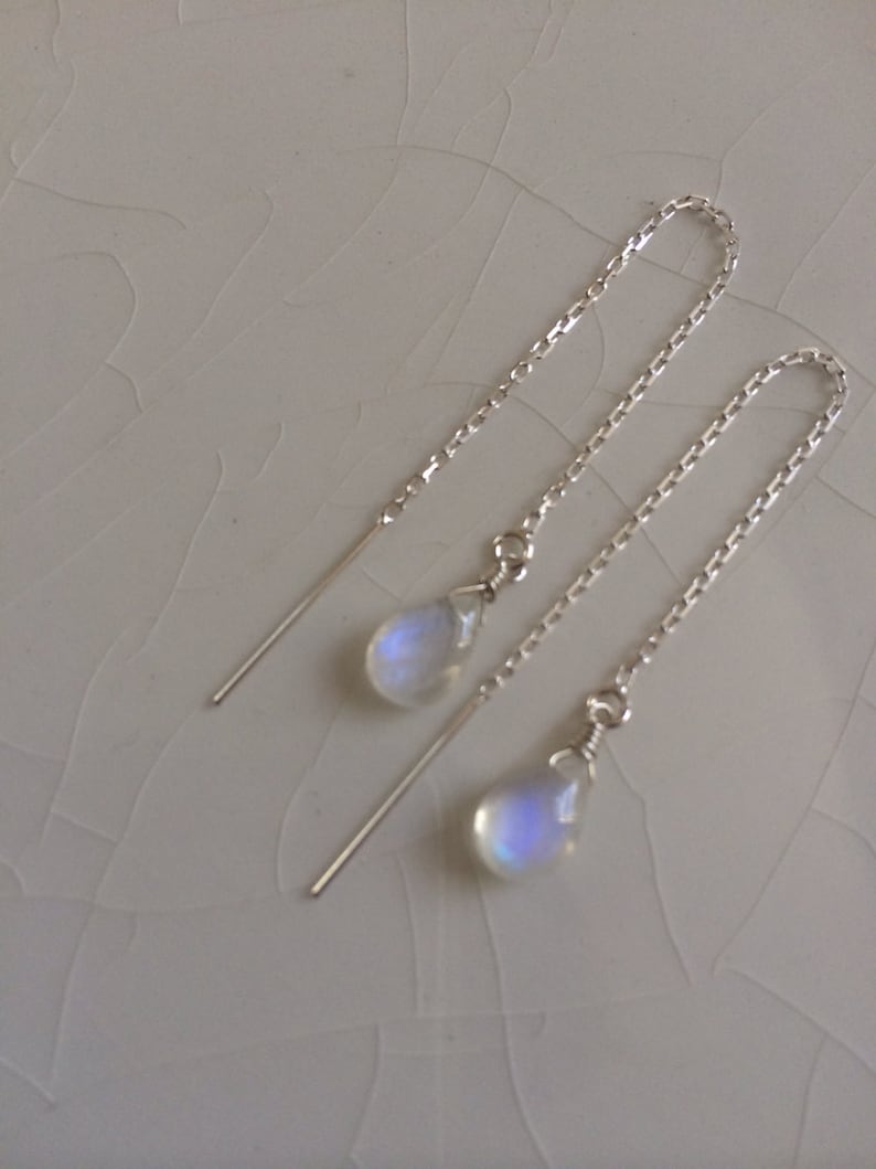 May include: A pair of silver dangle earrings with iridescent moonstone teardrop charms. The earrings have a delicate chain design.