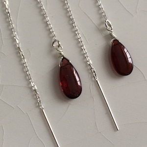 May include: A pair of silver chain earrings with a teardrop-shaped red gemstone pendant on each earring.