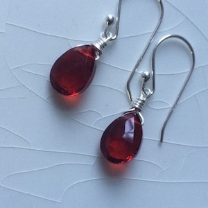 May include: A pair of silver dangle earrings with red teardrop-shaped gemstones.