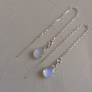 May include: A pair of silver chain earrings with a teardrop-shaped moonstone pendant on each earring.
