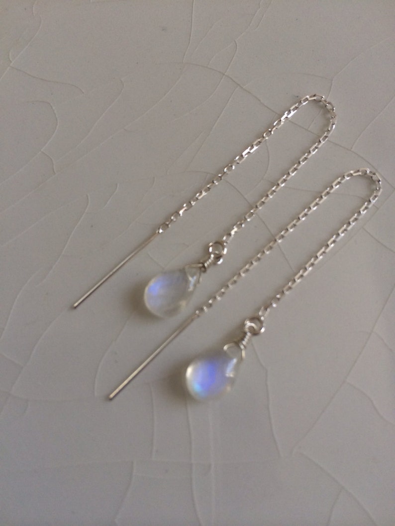 May include: A pair of silver chain earrings with a teardrop-shaped moonstone pendant on each earring.