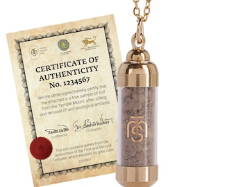 May include: A gold-colored necklace with a clear vial pendant filled with grey soil. The vial has a gold cap and a gold logo. A certificate of authenticity is visible, with text that reads "CERTIFICATE OF AUTHENTICITY No. 1234567".