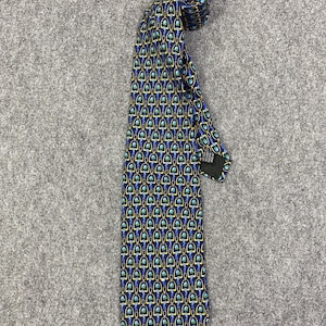 Könnte beinhalten: Eine marineblaue Krawatte mit einem sich wiederholenden Muster aus goldenen und türkisfarbenen Formen. Die Krawatte ist oben aufgerollt und liegt flach auf einer grauen Oberfläche. Das Muster ist eine Reihe verbundener Formen.