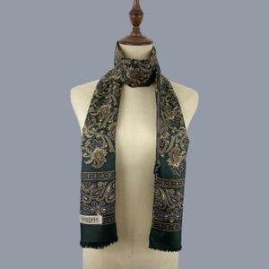 May include: A dark green scarf featuring a detailed paisley pattern in shades of gold, blue, and white. The scarf has a rectangular shape with fringed ends and a small white rectangular label near the bottom edge with the text LAUTREC PARIS.