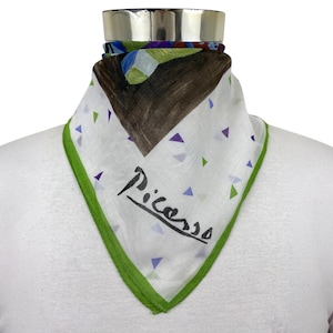 May include: A white triangular scarf featuring a green border and a pattern of small purple and green triangles. The scarf displays a large brown abstract shape at the top and the word Picasso written in black script across the lower section.