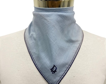 Può includere: Un foulard triangolare azzurro con un logo ricamato blu scuro sulla punta inferiore. Il tessuto presenta una trama visibile e i bordi sono rifiniti con un sottile bordo blu scuro che incornicia l'intera forma triangolare dell'accessorio.