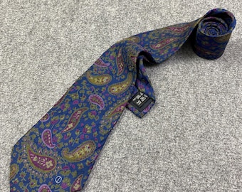 Könnte beinhalten: Eine blaue Paisley-Krawatte mit lila, gelben und grünen Akzenten. Die Krawatte ist am Ende aufgerollt und liegt auf einer grauen Oberfläche. Das Paisley-Muster ist ein klassisches Design, das sich für formelle oder halbformelle Anlässe eignet.