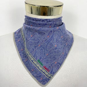 May include: A blue paisley patterned scarf with a grey border. The scarf features a repeating design of curved shapes and small pink dots. The text "MICIO GUCCI" is embroidered in green and red on the corner.