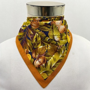 Peut inclure: Un foulard carré avec un imprimé botanique vibrant avec des feuilles vertes, des fruits bruns et des accents jaunes sur un fond bleu marine. Le foulard a une bordure orange et le mot "PLAYBOY" est visible.