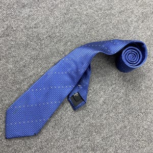 May include: A blue tie with a small square pattern. The tie is rolled up at the end and has a label that says "FEN". The tie is lying on a gray surface.
