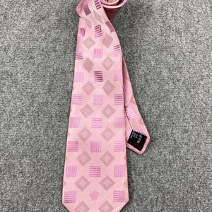 May include: A pink tie with a geometric pattern of squares and rectangles. The tie is made of a silky material and has a subtle sheen. The tie is rolled up at the top, and the bottom is spread out. The tie has a small tag on the back.