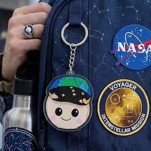 Puede incluir: Una taza de cerámica blanca con un asa negra y el texto "But First, Coffee" en negrita negra. La taza se encuentra sobre un fondo borroso, sugiriendo un ambiente acogedor.