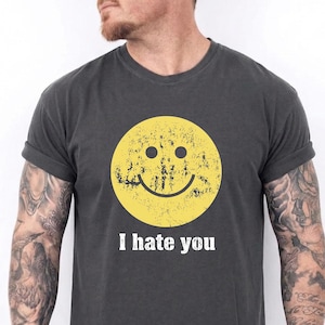 May include: Dark grey t-shirt with a distressed yellow smiley face graphic. The text "I hate you" is printed in white below the graphic. The shirt has rolled-up sleeves and a crew neck.