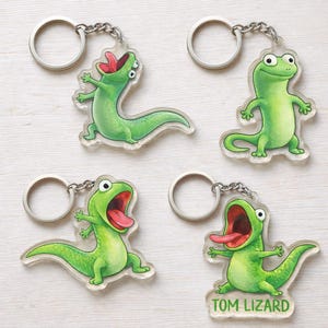 May include: Four clear acrylic keychains featuring cartoon green lizards with open mouths and red tongues. Each keychain has a silver metal ring and chain. One keychain has the text "TOM LIZARD".
