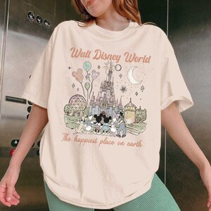 May include: A cream-coloured t-shirt with a graphic of Cinderella's castle, Mickey Mouse, and other Disney characters. The text "Walt Disney World" and "The happiest place on earth" are printed above and below the graphic in a vintage style.
