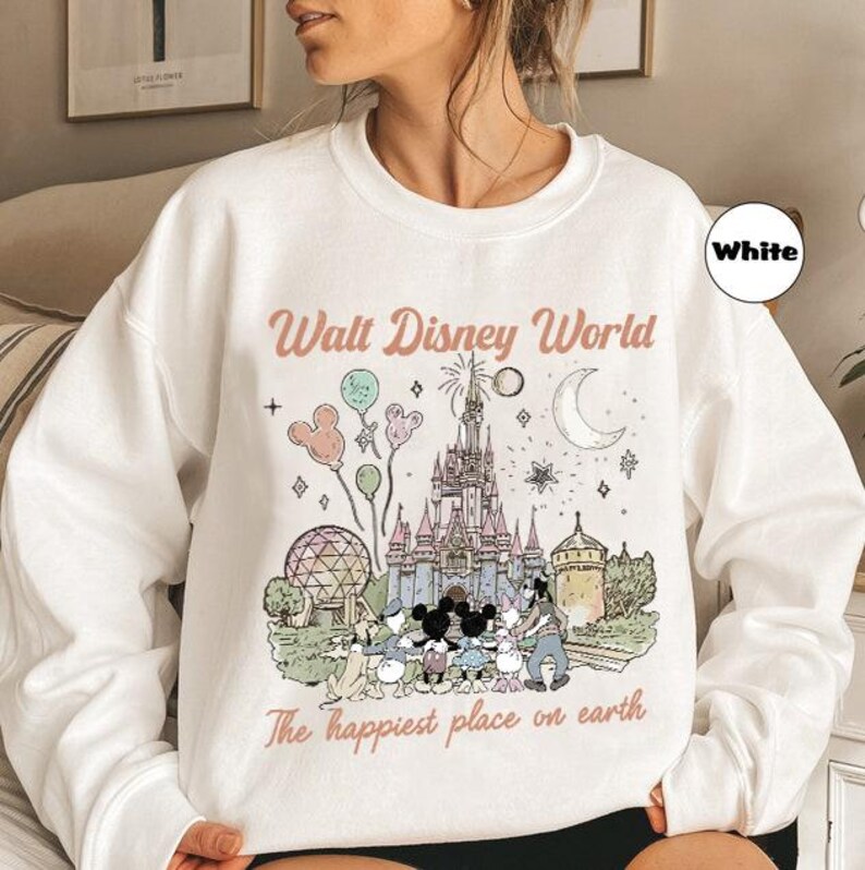 May include: White sweatshirt with a graphic of Cinderella's castle, Mickey Mouse, and other Disney characters. The text "Walt Disney World" and "The happiest place on earth" are printed on the front.