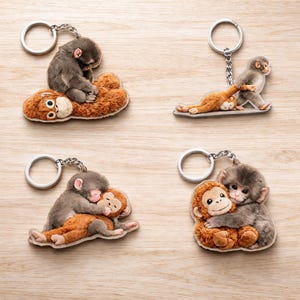 May include: Four keychains with monkey designs. Each keychain features a silver ring and chain. The monkey designs include a gray monkey hugging a brown monkey, a gray monkey on top of a brown monkey, and a gray monkey pulling a brown monkey.