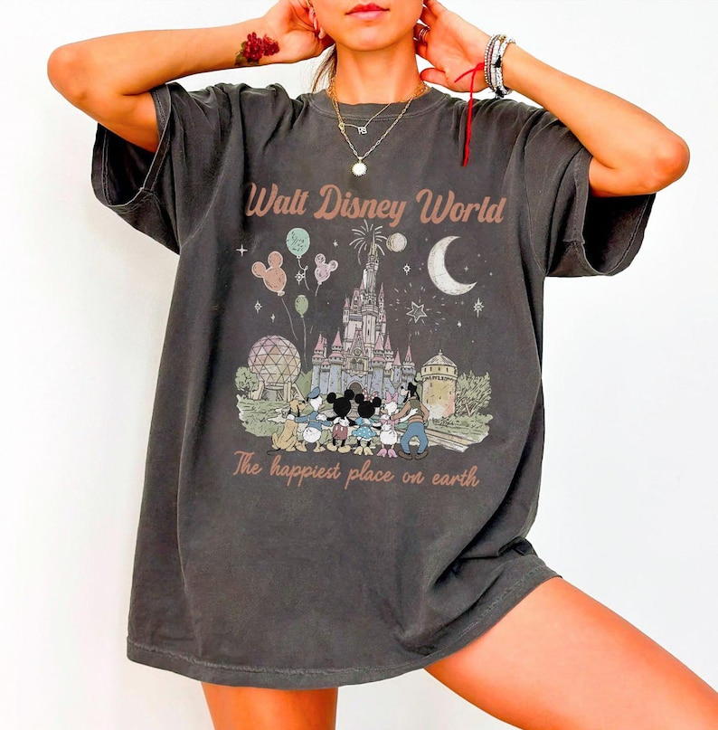 May include: Dark grey t-shirt with a vintage-style Walt Disney World graphic. The design features the castle, Mickey Mouse and friends, balloons, and the text "The happiest place on earth."