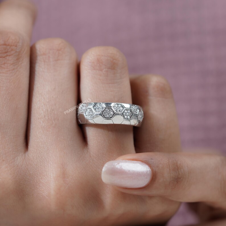 May include: A silver ring with a honeycomb design, featuring small, clear gemstones set within each hexagonal cell. The ring is shown on a finger, with the brand name "PRASHIV JEWELS" visible.