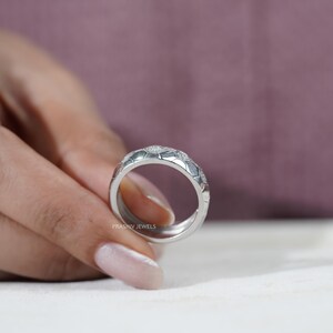 May include: A silver ring with a geometric pattern of small, sparkling stones. The ring's design features a series of interconnected shapes, creating a textured surface. The ring is held by a person, with the brand name "PRASHIV JEWELS" visible.