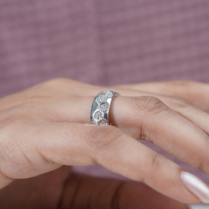 May include: A silver ring with a honeycomb design, set with small, sparkling stones. The ring is on a finger, with the brand name "PRASHIN JEWELS" visible. The ring's design is a series of connected hexagons, each filled with a cluster of small stones.