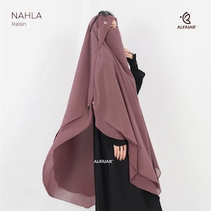 Könnte beinhalten: Ein rosafarbenes Nahla-Hijab mit einem geschichteten Design. Die Kopfbedeckung hat einen Gesichtsschleier und wird mit einem schwarzen Kleidungsstück kombiniert. Das Markenlogo "ALFAJAR" ist sichtbar. Das Wort "Nahla" ist oben links aufgedruckt.