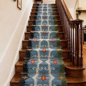 Puede incluir: Una alfombra azul para escaleras con un patrón geométrico en blanco, rojo y amarillo. La alfombra está instalada en escaleras de madera con un acabado marrón oscuro. La alfombra tiene flecos en la parte inferior y barras de latón.