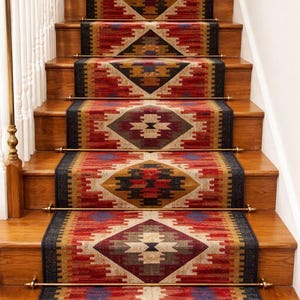 Puede incluir: Escalera de madera con alfombras estampadas. Las alfombras presentan un diseño geométrico en rojo, negro, dorado y beige. Barras de latón aseguran las alfombras a los escalones. La estética general es cálida y acogedora.
