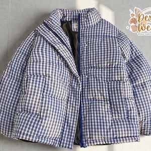 May include: A blue and white checkered puffer jacket with a high collar and a zipper closure. The jacket has a quilted design and two pockets. The "Desert Weave" logo is visible in the upper right corner.