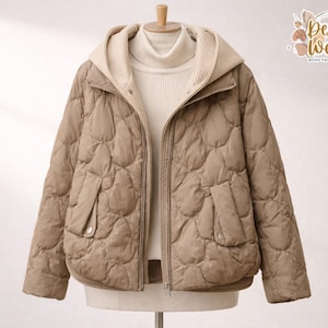 Puede incluir: Chaqueta acolchada color beige con capucha crema y jersey de cuello alto a juego. La chaqueta tiene cierre de cremallera y dos bolsillos delanteros. La chaqueta se exhibe en un maniquí. El logo de la marca "Desert Weave" es visible.