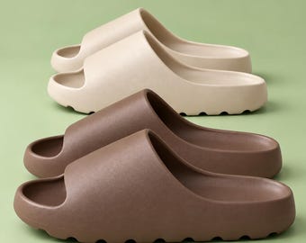 May include: Two pairs of slip-on sandals are displayed. One pair is a light beige color, and the other pair is a dark brown color. Both pairs feature a wide, single-strap design with a thick, contoured sole and a rounded, open-toe front.