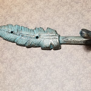 May include: A turquoise and silver cast iron feather hook. The hook is shaped like a feather with a curved hook at the end.