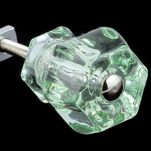 Pode incluir: Um botão de armário de vidro transparente verde com um parafuso de metal prateado e uma base de metal prateado.