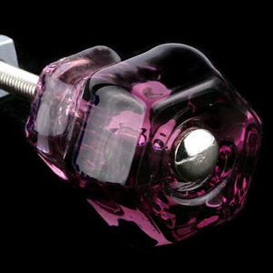 May include: A purple glass cabinet knob with a silver metal screw. The knob has a faceted design and a round, silver metal base.