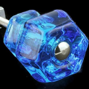 May include: A blue glass cabinet knob with a silver screw. The knob has a hexagonal shape and a textured surface.