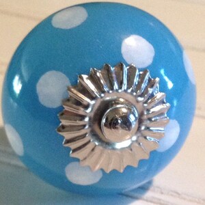 May include: A blue ceramic knob with white polka dots and a silver metal accent. The knob is round and has a smooth surface.