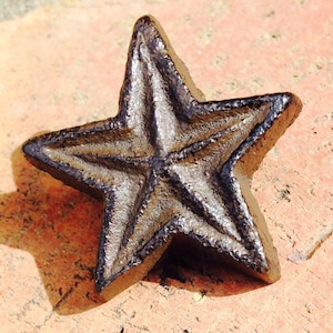 Könnte beinhalten: Ein gusseiserner Stern mit einer rustikalen braunen Oberfläche. Der Stern hat ein fünfzackiges Design mit einer erhöhten Mittelspitze.