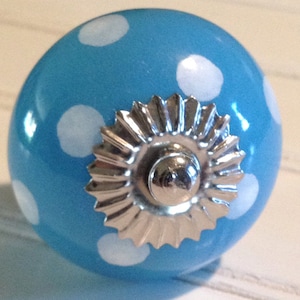 Puede incluir: Un pomo de cerámica azul con lunares blancos y una base de metal plateado.