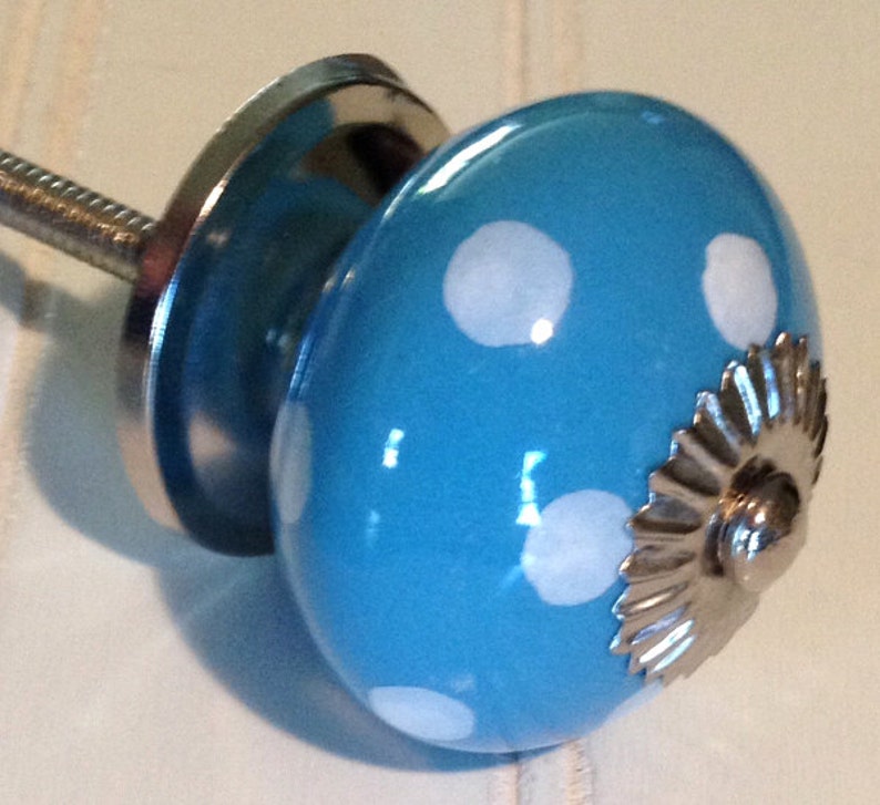 May include: A blue ceramic knob with white polka dots and a silver metal base. The knob has a decorative, scalloped edge.