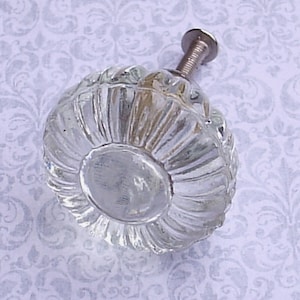 May include: Clear glass cabinet knob with a ribbed, rounded design. The knob has a silver-colored screw for attachment. The glass is transparent, allowing light to pass through. A decorative hardware item.