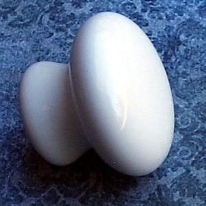 May include: White ceramic knob with a rounded oval shape. The knob has a smooth, glossy finish.
