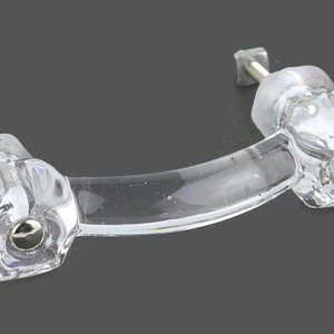 May include: Clear glass cabinet door pull with a curved bar and octagonal knobs. The knobs have a faceted design and a silver metal screw.