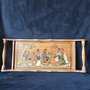Könnte beinhalten: Serviertablett aus Holz mit handgemalter, asiatisch inspirierter Szene. Das Tablett hat ein rechteckiges Design mit abgerundeten Griffen. Das Kunstwerk zeigt Figuren in traditioneller Kleidung, Bäume und Landschaften.