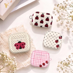 May include: Four protective cases for wireless earbuds featuring ladybug designs. One case has a white background with a ladybug pattern, one has a cream background with black polka dots and a large ladybug, one has white with black dots and small ladybugs, and one has a pink gingham pattern with small ladybugs.