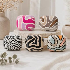 May include: Five rectangular earbud cases featuring various abstract wavy patterns. The top left case is pink and purple, the top right is brown and beige, the bottom left is black and white, the bottom center is black and tan, and the bottom right is multicolored.